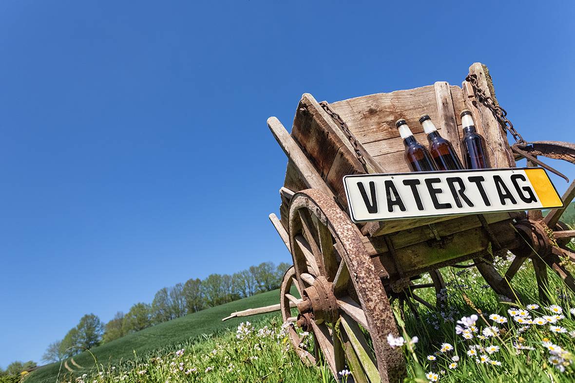 Ein alter Bollerwagen mit Bierflaschen auf einer Wiese mit einem Schild auf dem Vatertag steht